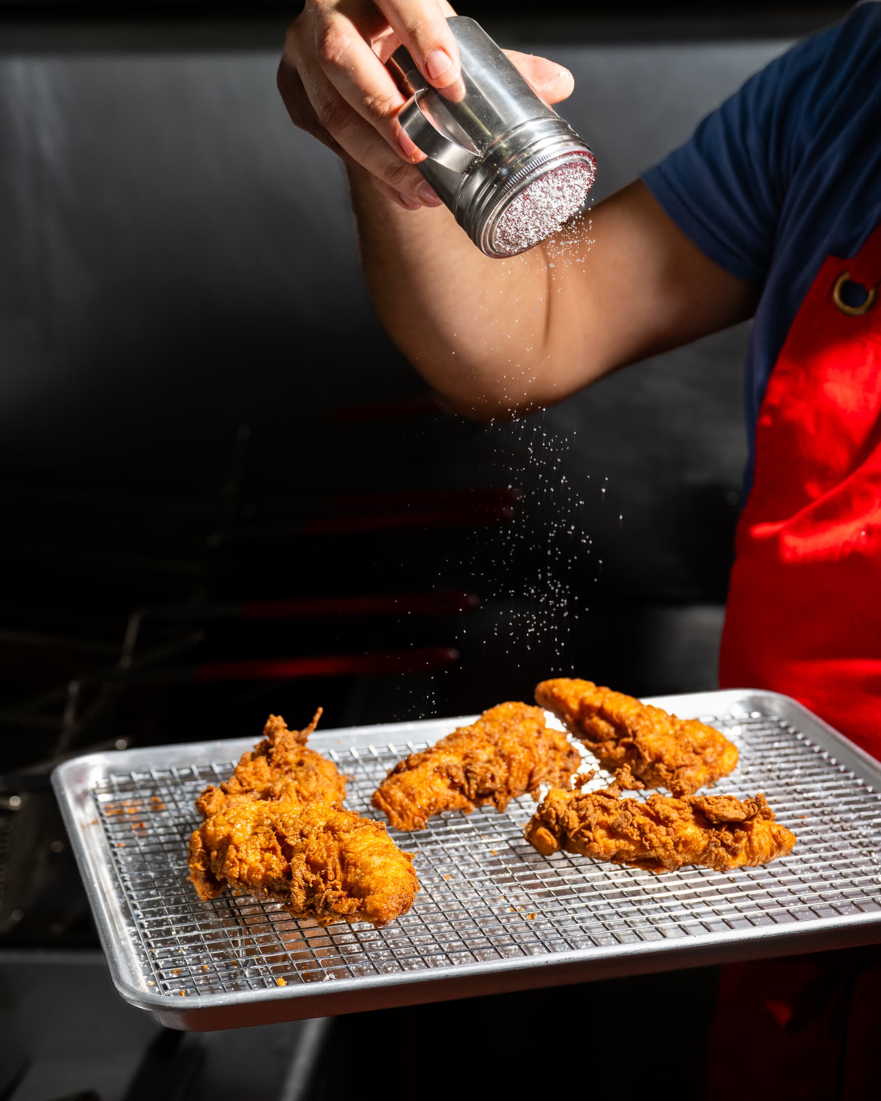 Freshly fried chicken being seasoned with salt